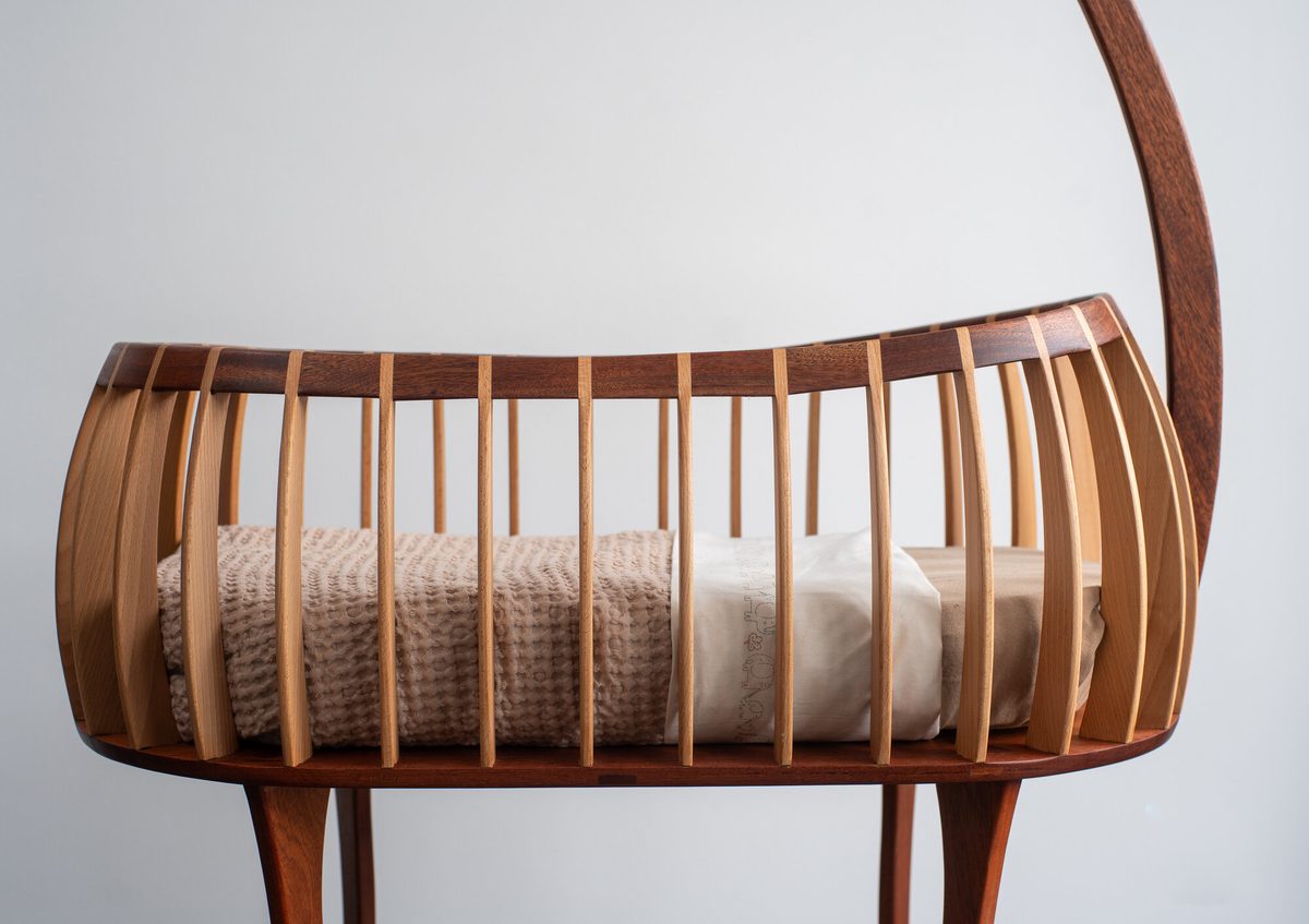 De mand van de handgemaakte wieg met beuken spijlen en mahonie rand, gedekt met wollen dekentje